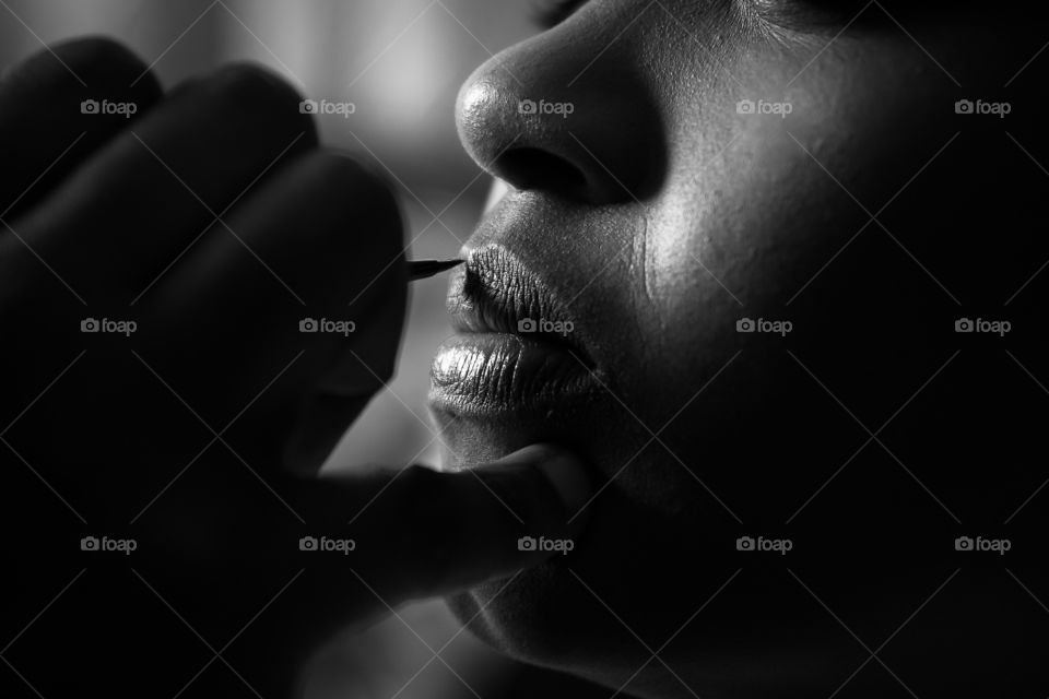 Make up is an essential part of my daily routine. Image of woman putting on lipstick. Monochrome image.