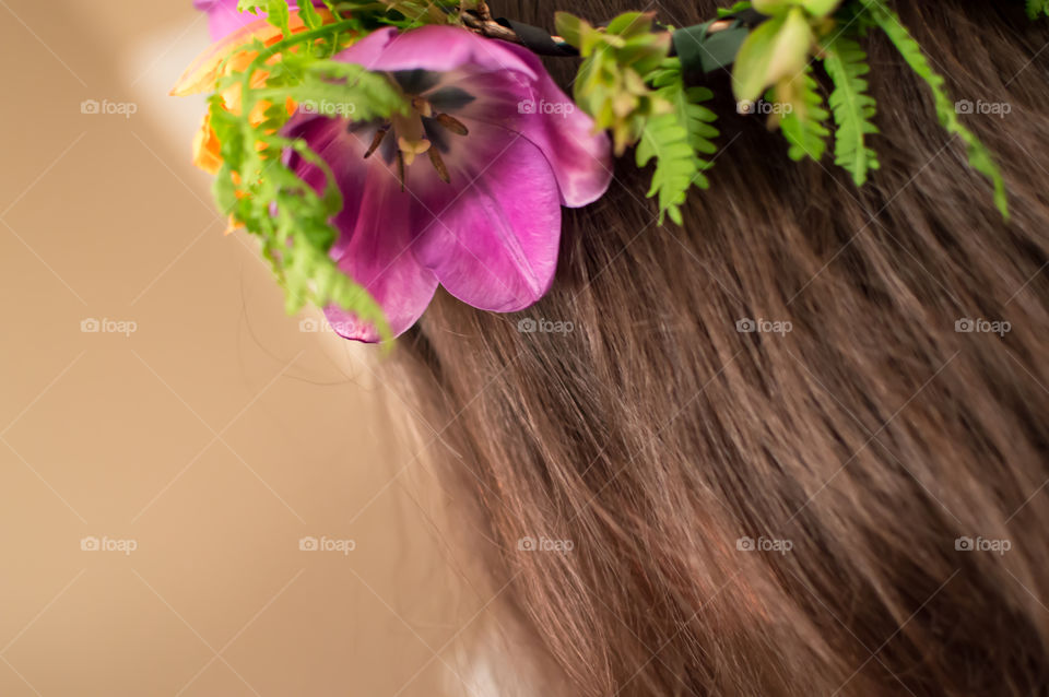 Flower garland in long brown hair rear angle view of woman facing forward closeup on hair with flowers and ferns on crown 