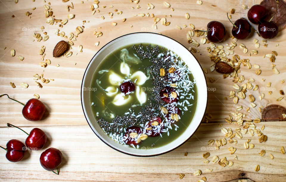 Beautiful artisanal green smoothie bowl photography conceptual healthy lifestyle background with elegant garnish items chia, oatmeal,dark cherry sliced, yogurt, coconut sprinkles, almonds and honey  and fresh fruit ingredients 