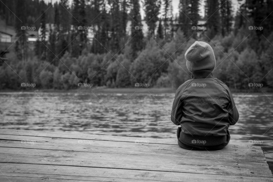 alone. kid's seating alone near a lake