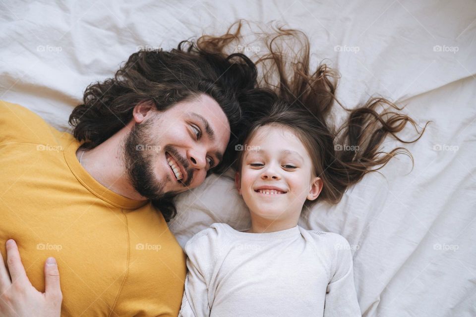 Happy father young man and girl little daughter having fun on bed in at home