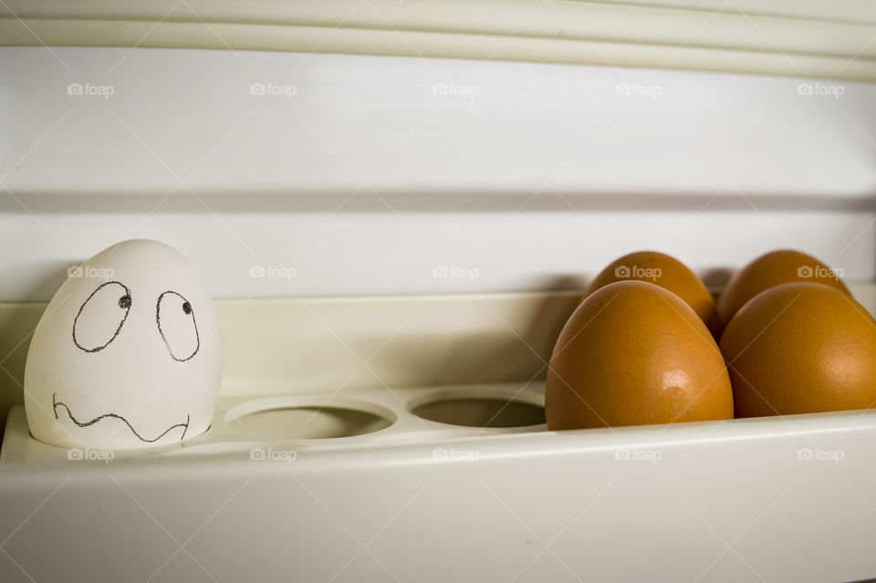 a white egg lies on one shelf with brown eggs in the refrigerator