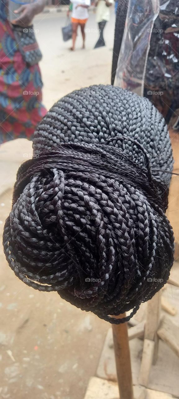 Beautiful Head of African hair braids on a stick with passerbys on the street admiring it.