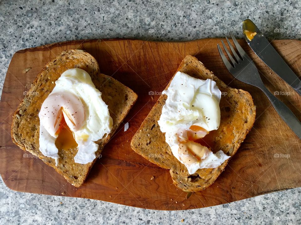 Poached eggs on toast on olive wood with cutlery 