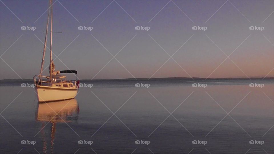 Yacht floating off the Australian coast at sunset, reflecting on the water on a picturesque evening.