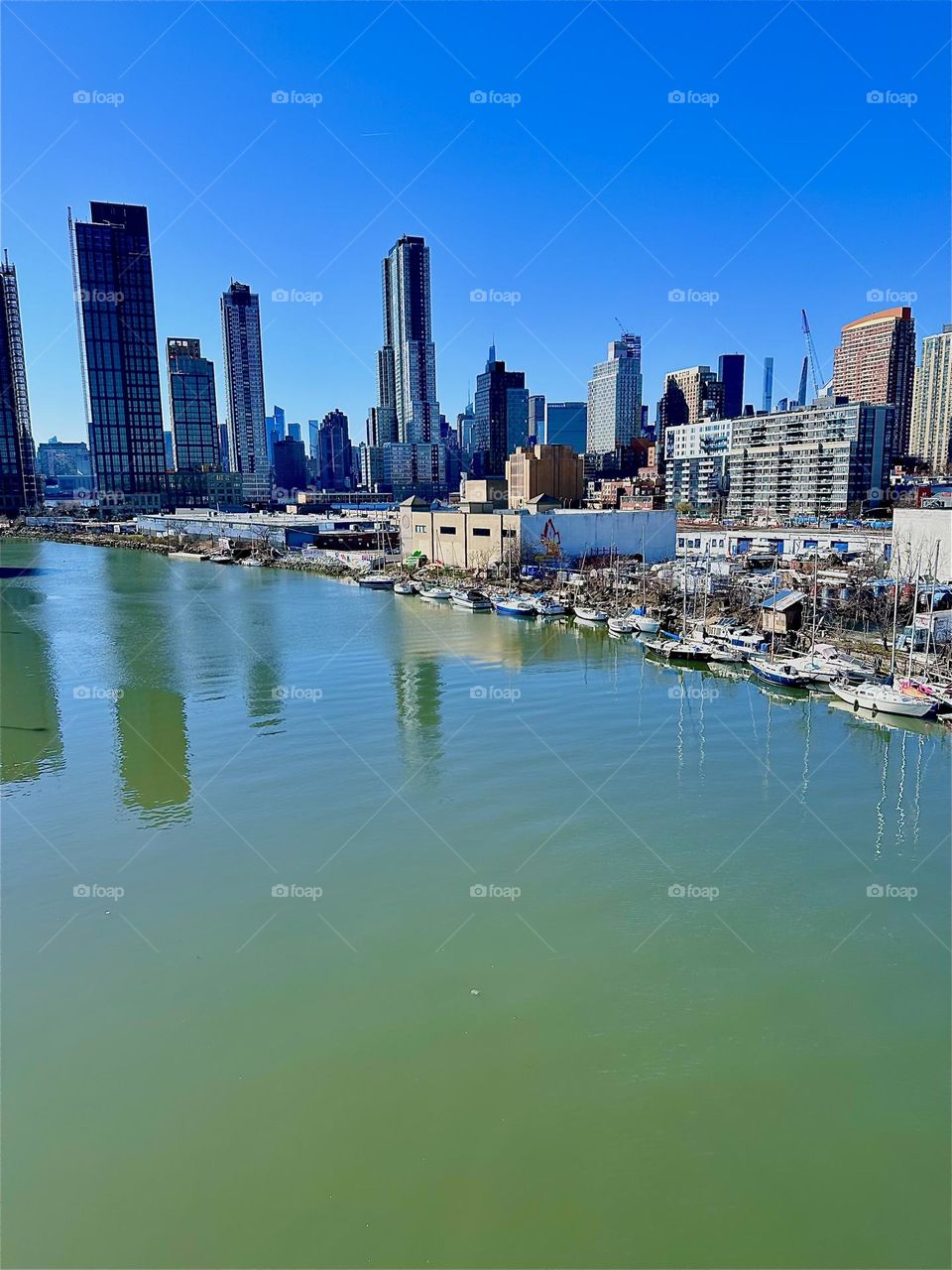 This is beautiful „Newtown Creek“ with its many boats seen from the „Pulaski Bridge“ that connects LIC, Queens „Greenpoint“, Brooklyn. In the distance behind the LIC high rises we can see „Manhattan“. 2024. Hypnotic Productions