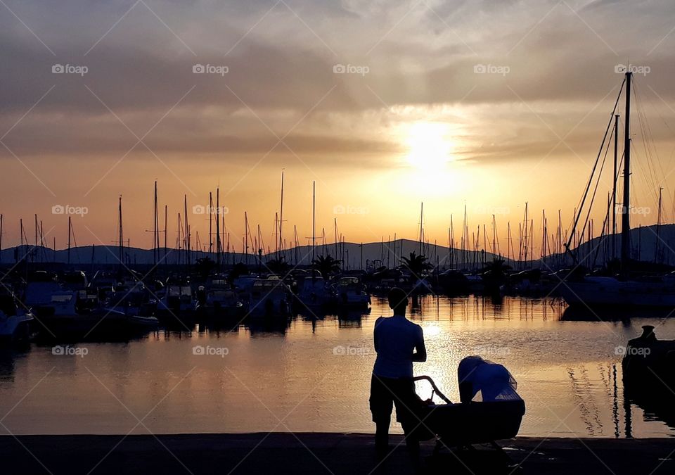 doppietta of mom with baby, staring at the sunset over marina. shot by phone