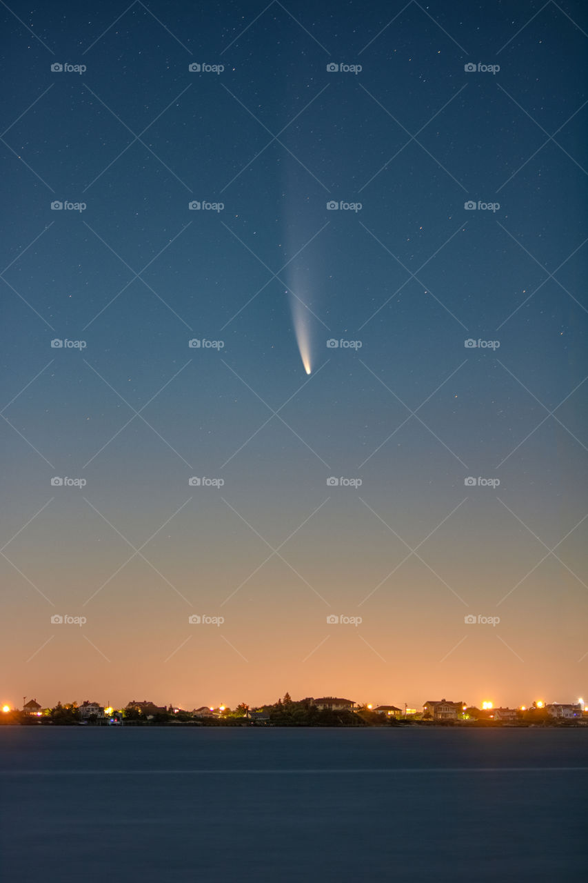 Comet NEOWISE streaking through the night sky, as pre dawn golden light illuminates the horizen. 