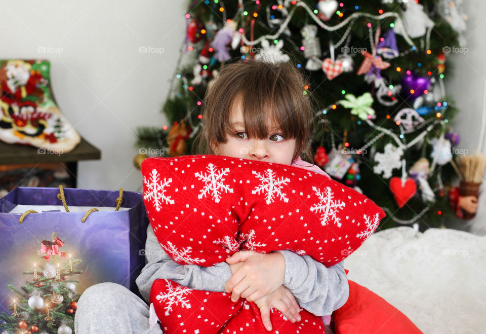 Little girl holding pillow in front Christmas tree