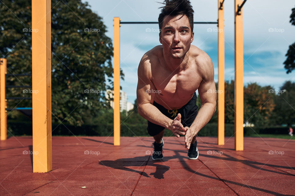 Young shirtless man bodybuilder doing clapping push-ups on a red rubber ground during his workout in a modern calisthenics street workout park