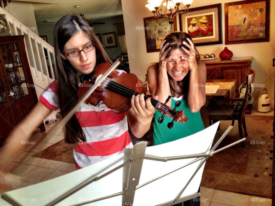 Young girl playing the violin in the house while mother covers her