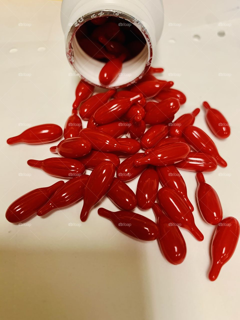 Beautiful shiny red vitamin A capsules, spilled from a bottle onto a white paper.