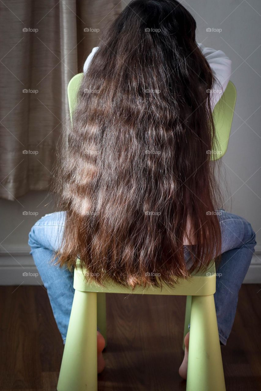 Girl with wonderful long healthy hair is sitting on a kid's chair