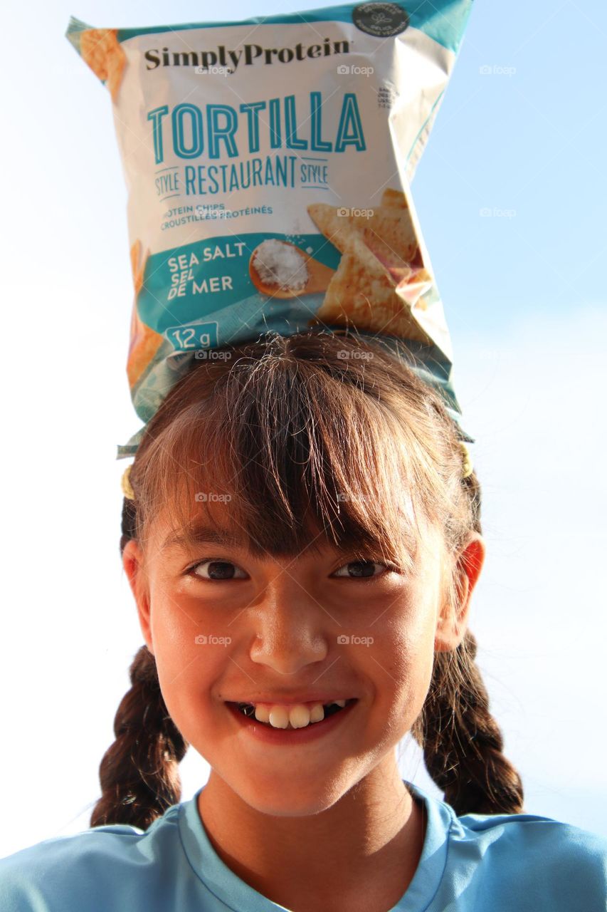 Cute happy girl is balancing bag of chips on her head