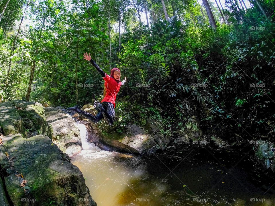 A happy girl jumping into a stream in a rainforest in Malaysia