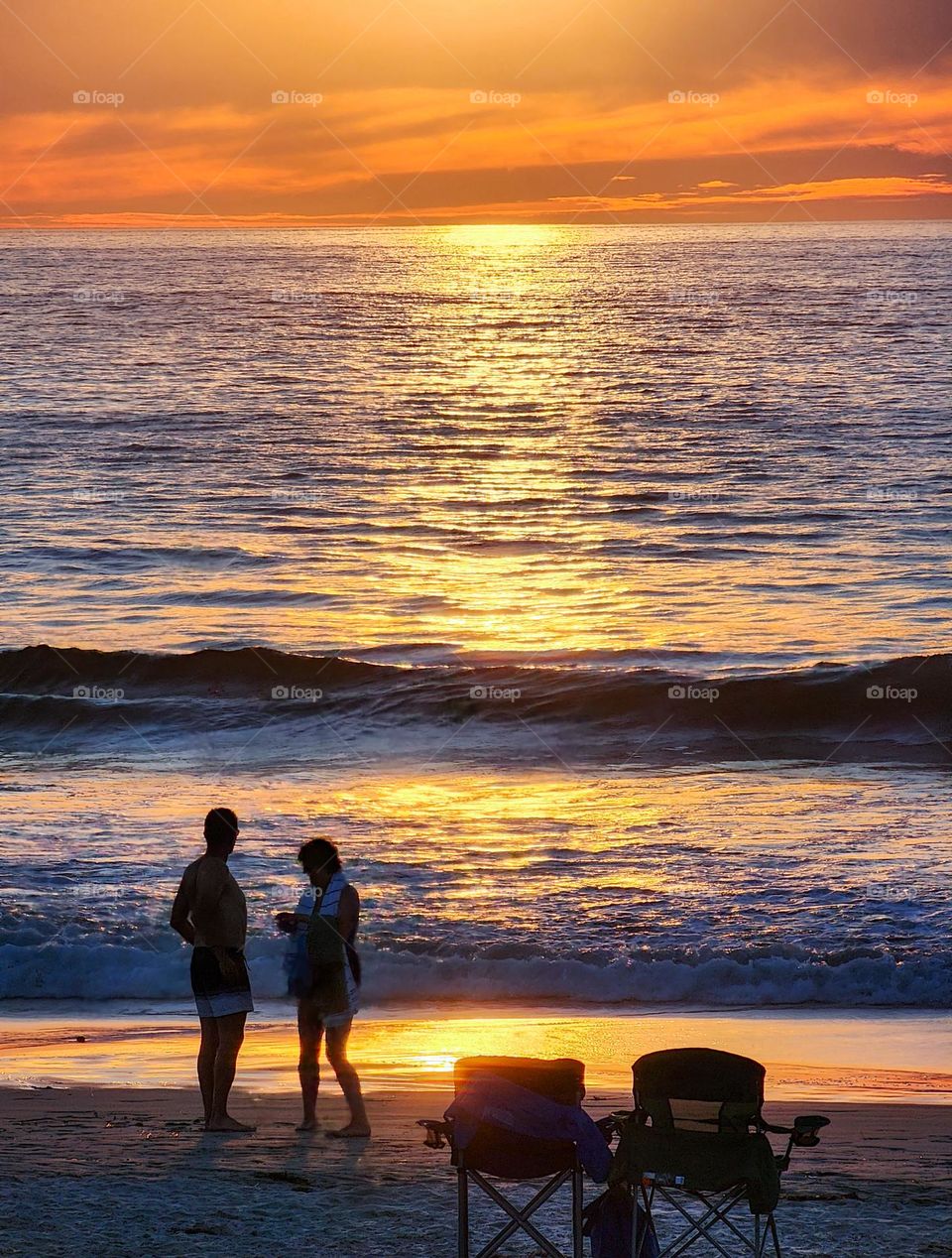 A couple enjoys a spectacular golden sunset on a beach in San Diego California on a warm evening