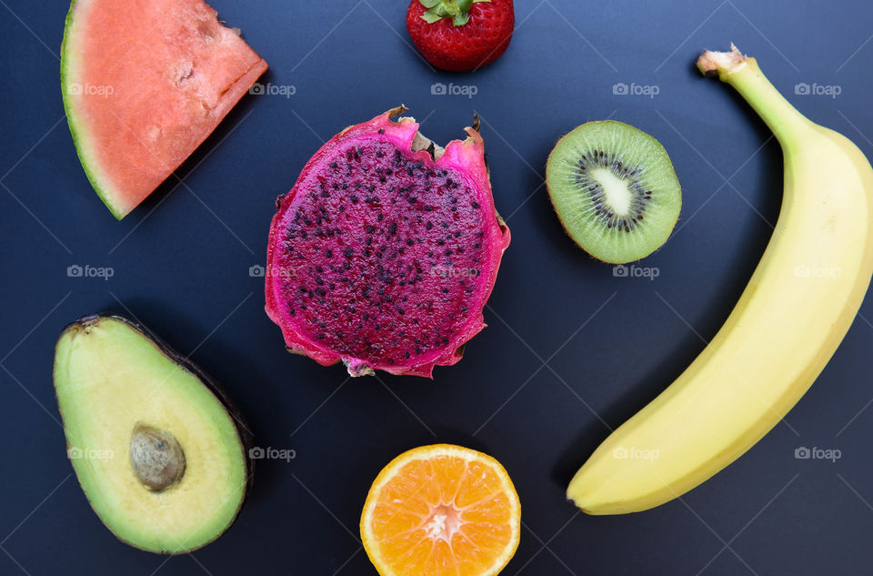 Flat lay of halved brightly colored fruits against a black background