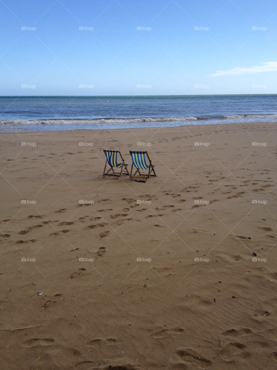 Two deck chairs on the beach by the sea with footprints in the sand, a calm lazy day getting ready for the sun to set 