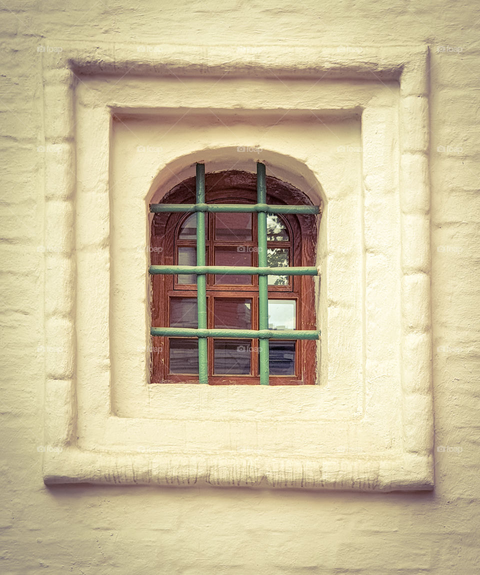 exterior of a barred window with a white brick wall of an old orthodox russian church