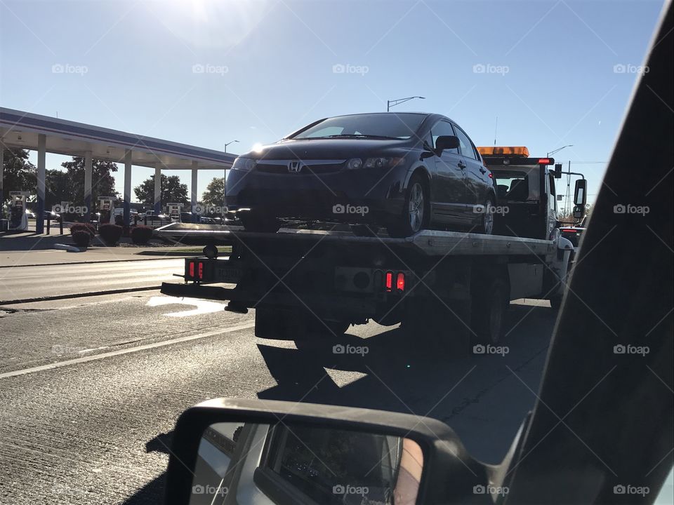 Stopped at a red light while driving, looking out the window and seeing a tow truck and a gas station.