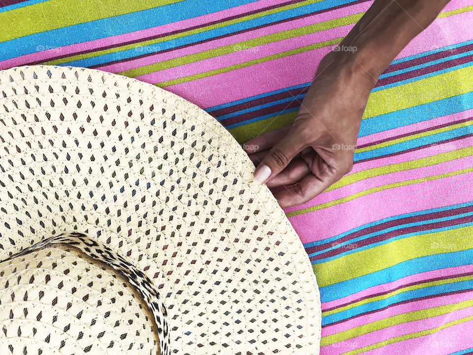 Female hand taking a beach hat from the colorful striped beach blanket 