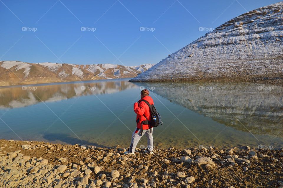 man traveler stands on the shore of a mountain lake among the snow-capped mountains of Pamir Asia