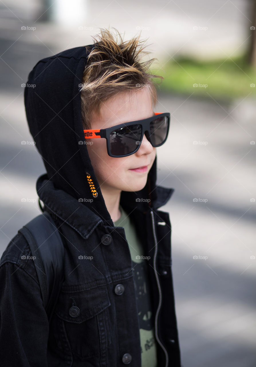 stylish boy in black clothes and glasses is walking along the street.  baby five years old, beautiful blond