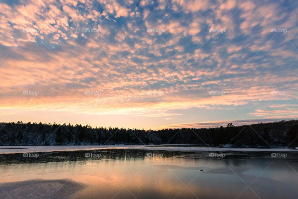 Beautiful glowing clouds at sunset over partly frozen lake 