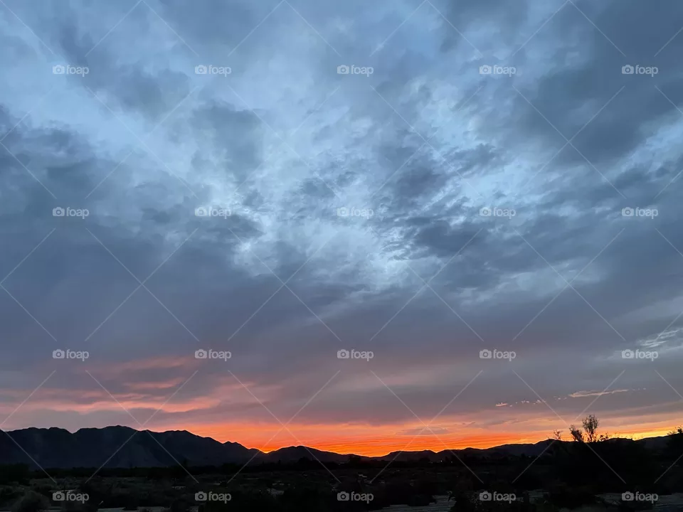 A colorful bright red sunset with clouds above it and mountains below it. 
