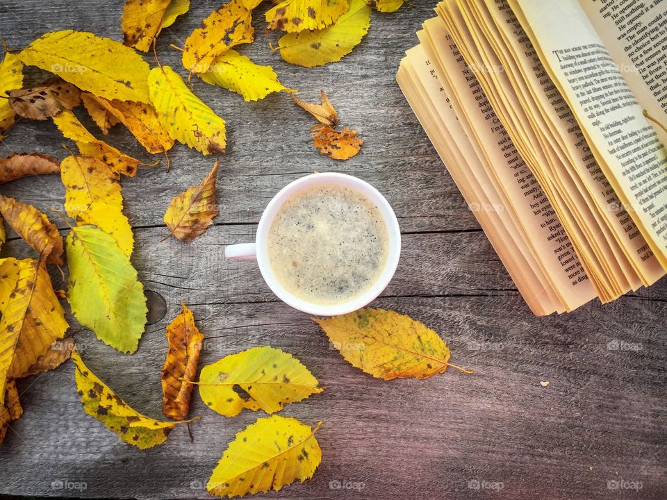 Cup of coffee on wooden table with a book and yellow autumn leaves beside