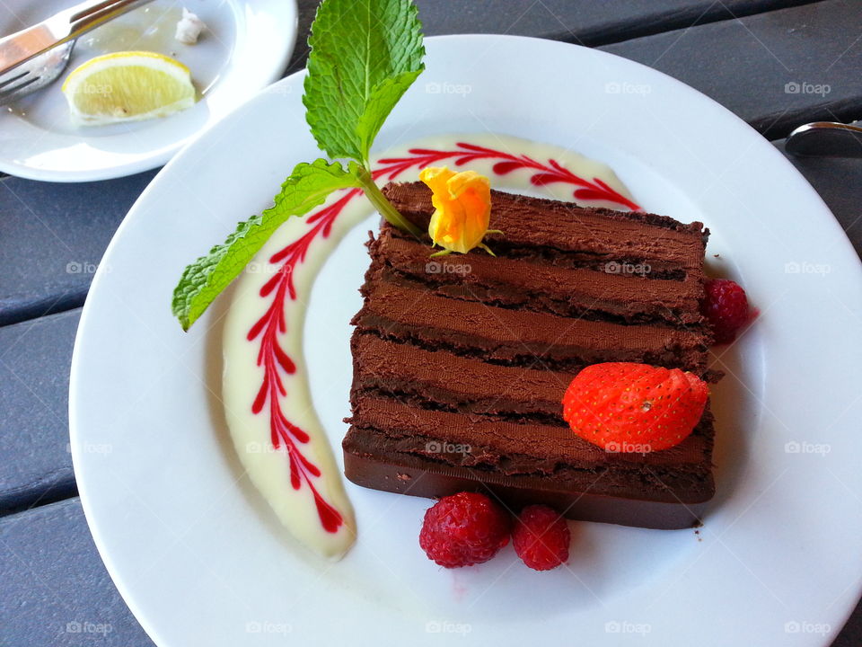 chocolate gluten-free cake with tropical garnish, raspberry, cream and raspberry on plate