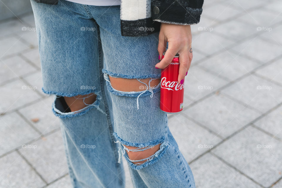 a girl in blue jeans holds a can of coca-cola in her hands, walks on the street