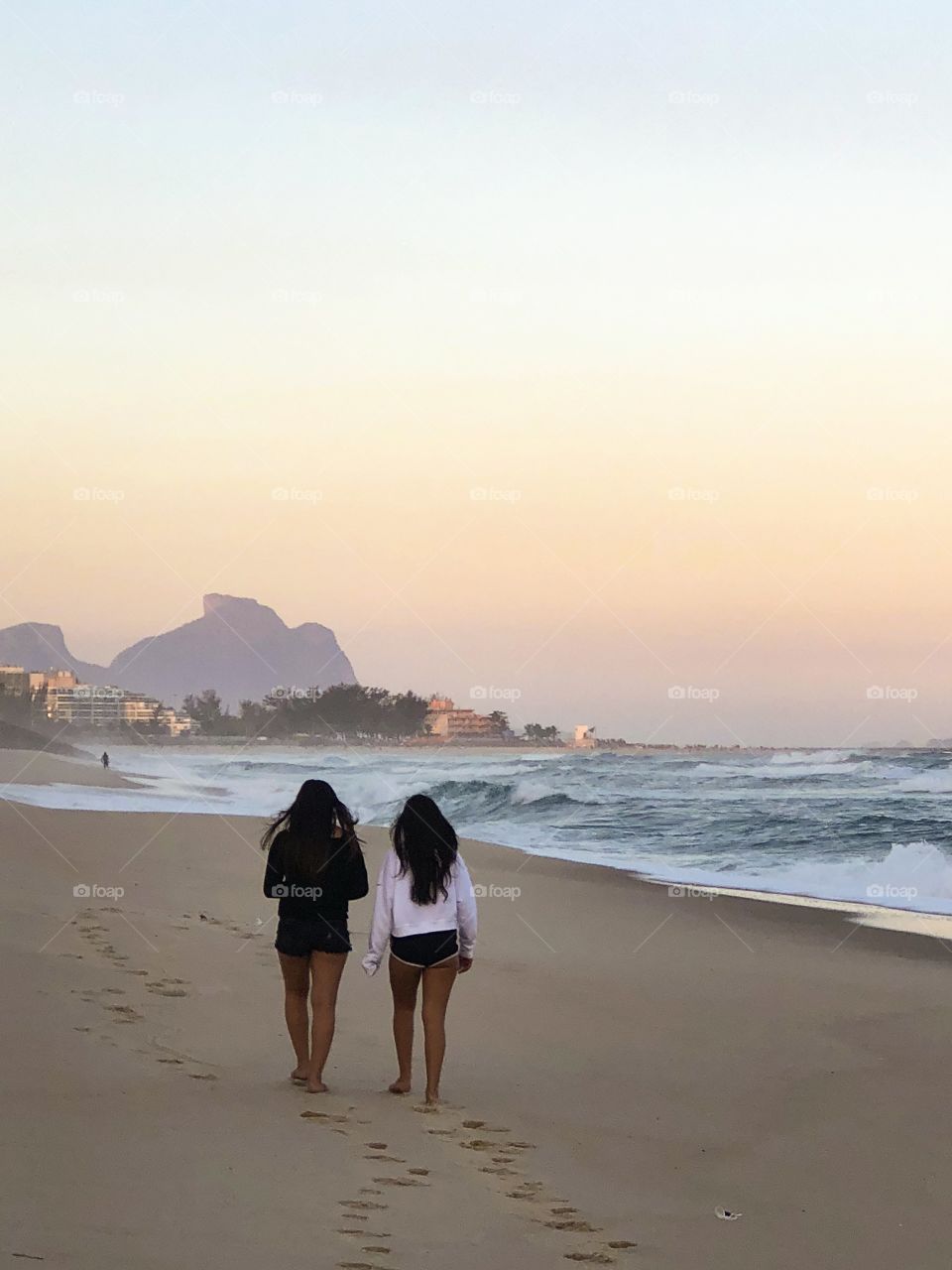 Two girls walking on the sand of a beach with beautiful view on a colorful sunset