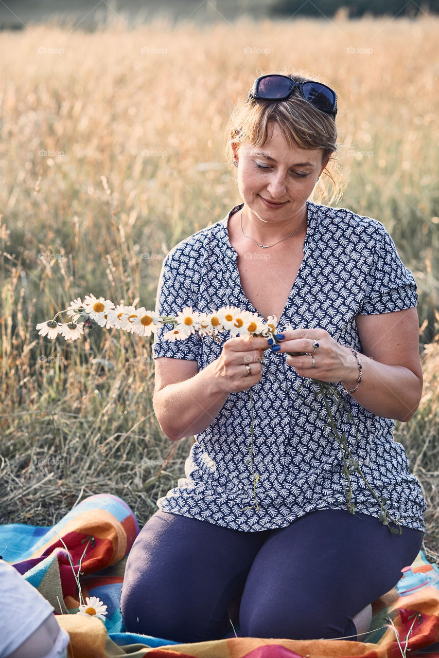 Smiling happy woman making coronet of wild flowers. Family spending time together on a meadow, close to nature. Candid people, real moments, authentic situations