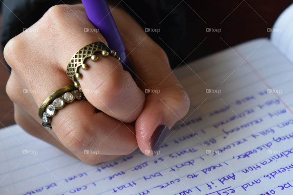 woman writing in a notebook with purple pen. wearing a crown ring. with purple nail polish .