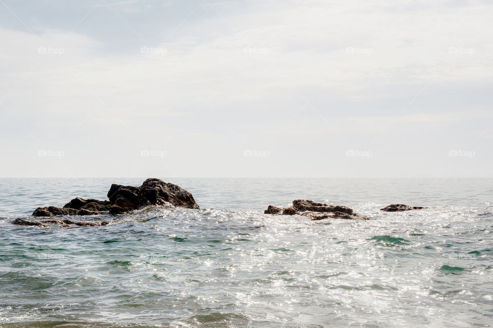 Rocks emerging from calm sea during sunny day.