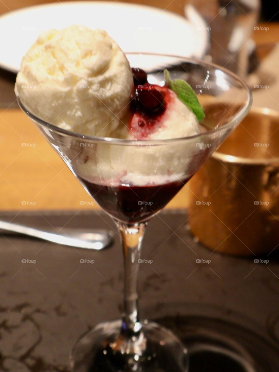 A delicious dessert served in a martini glass, with a scoop of vanilla ice cream covered with a red fruit sauce and decorated with a mint leaf, perfect for candy lovers.