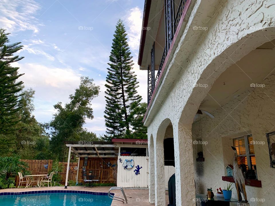 Gated white and red spanish old style architecture residential large house built in the early 1900s. Charming pretty style and beautiful landscaping with pool and chairs with great setting in a tropical environment with arched openings in patio area.