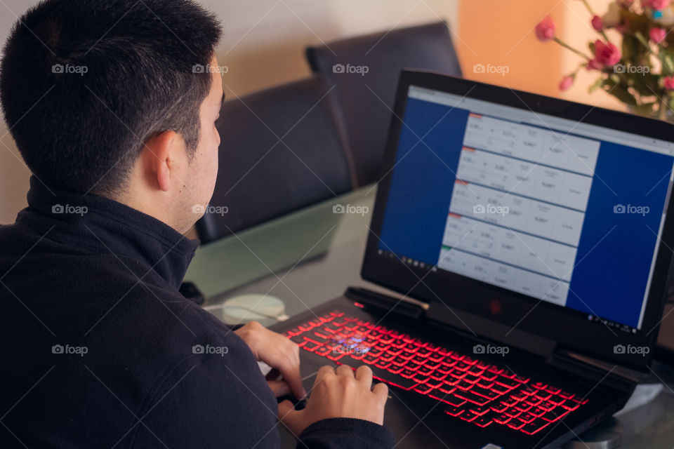 Young businessman using his red and black laptop to work at home 