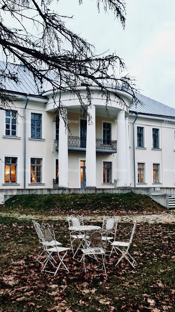 Large white mansion with columns and garden furniture on the front lawn