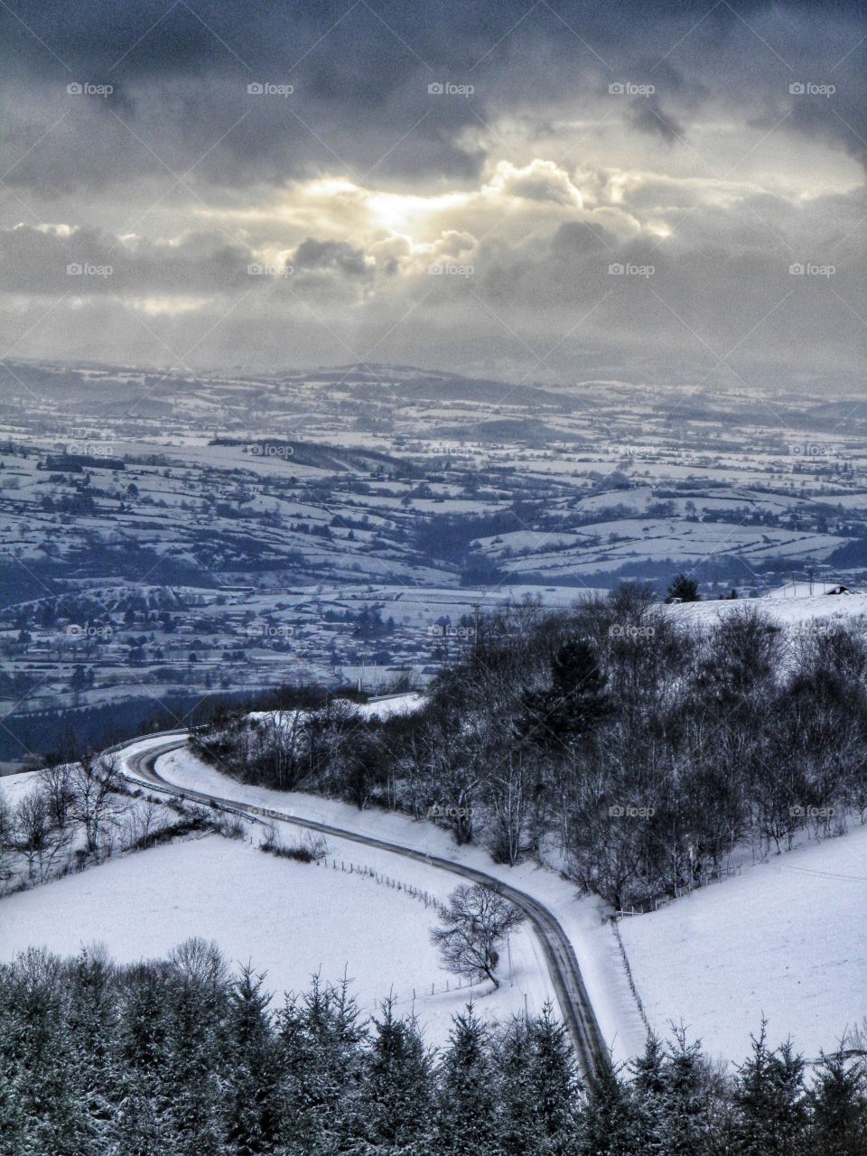 Route surplombant un paysage enneigé avec un rayon de soleil à travers les nuages