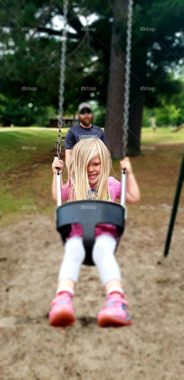 child smiling while swinging at a park on a nice summer day in Minnesota, blurred background.