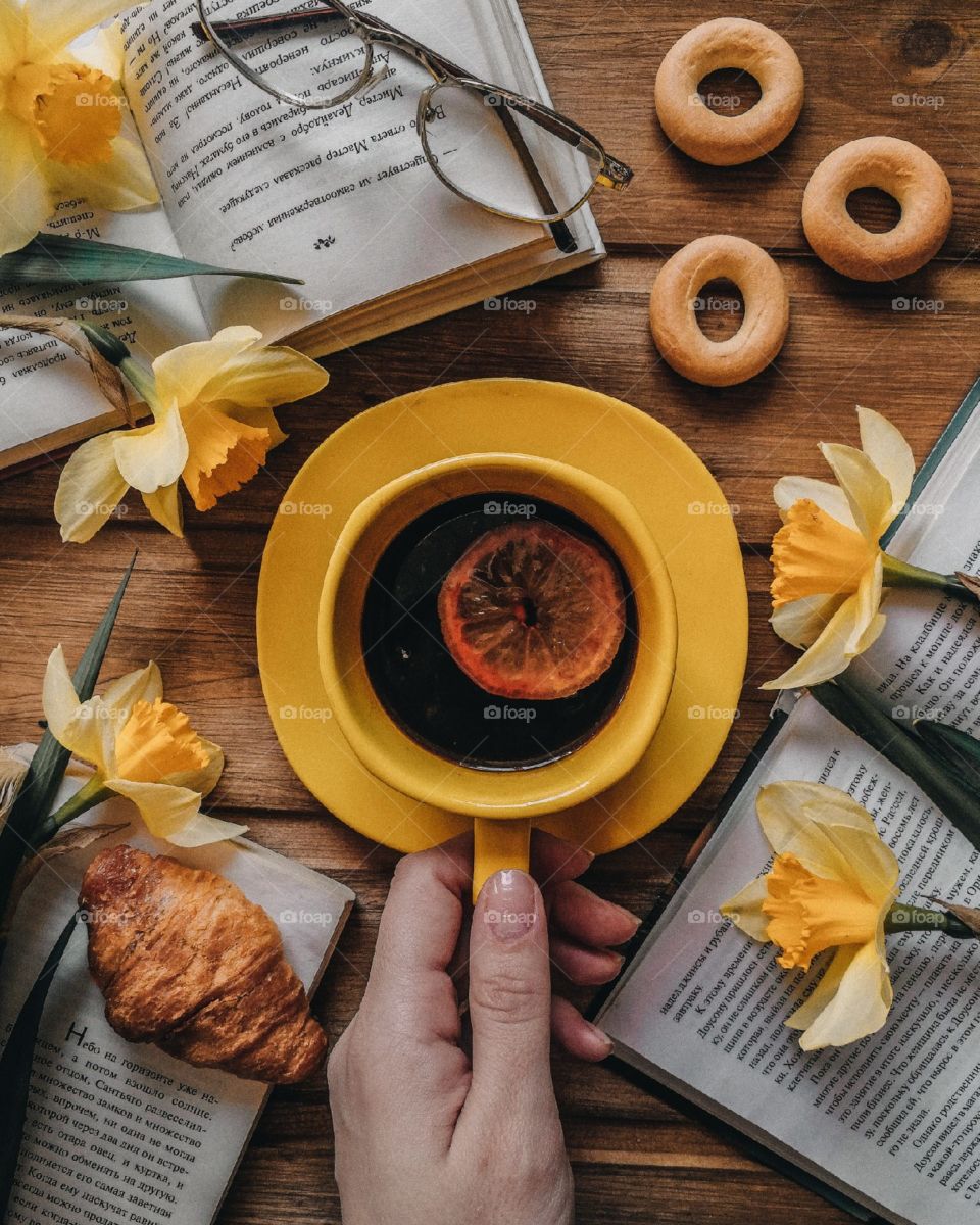 Breakfast flat lay with coffee, croissant, books and yellow fliwers