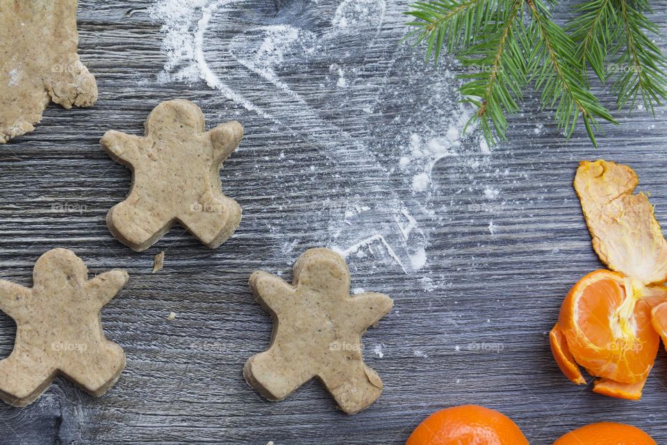 Cooking Christmas gingerbread cookies on a wooden table with tangerines and green Christmas trees.