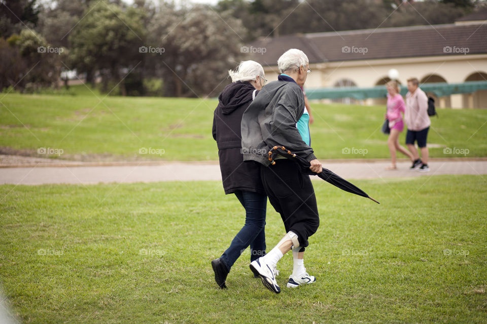 Old man and old woman, walking side by side, gray haired couple, taking a stroll at the beach park, elderly from behind