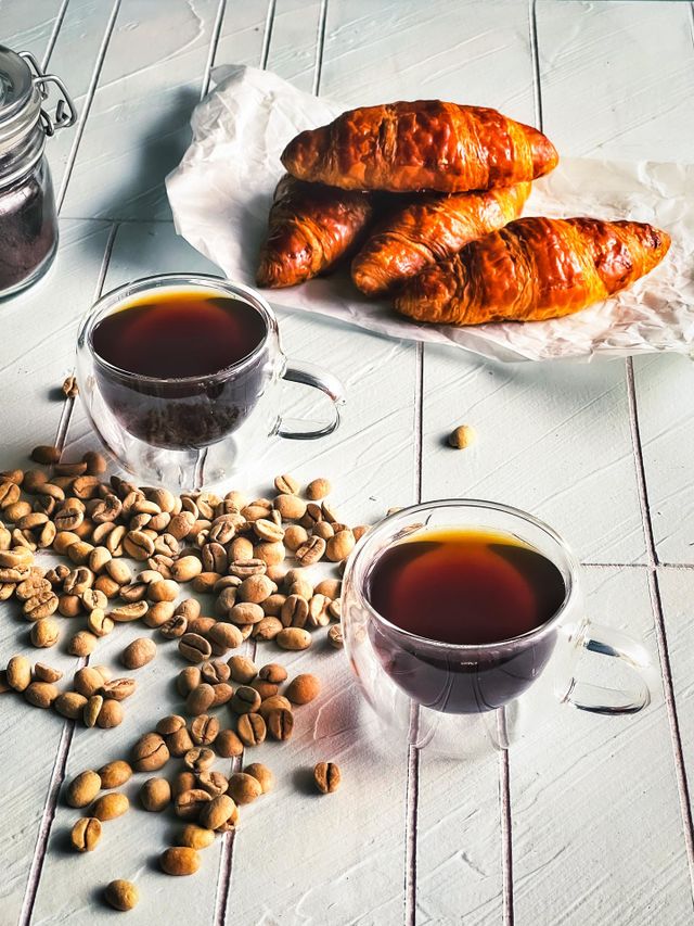 Hot coffee in cups for the winter, croissants at the back and coffee beans scattered at the side