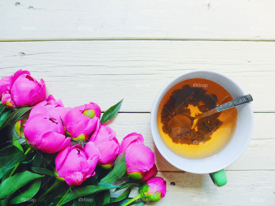 pink peony flowers and a cup of green tea on a white background