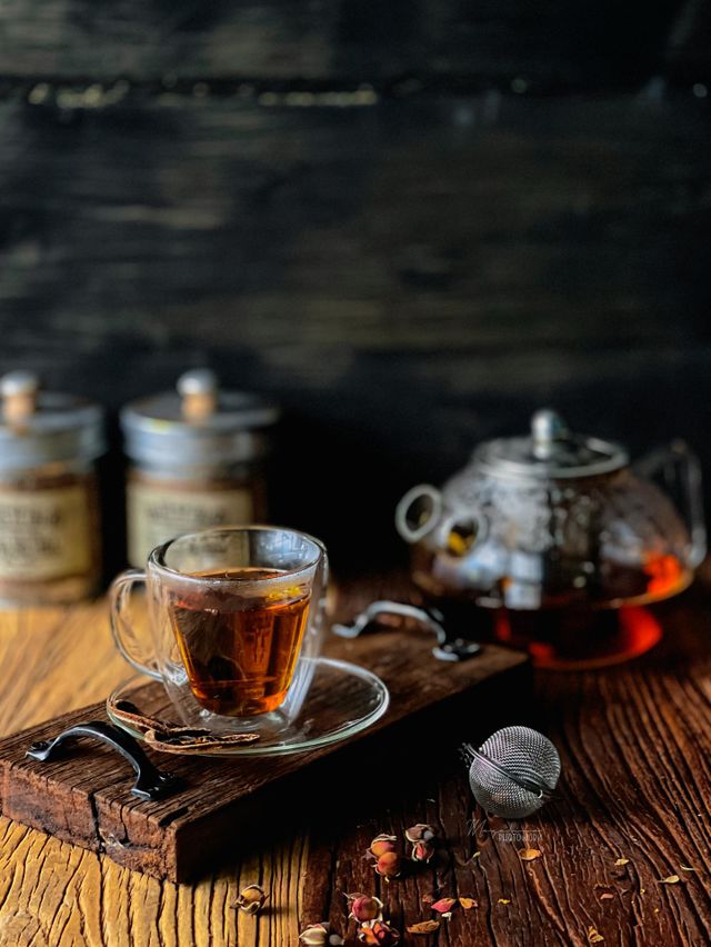 Tea time; a cup of tea on a wooden board and some dried flower scattered on the wooden table
