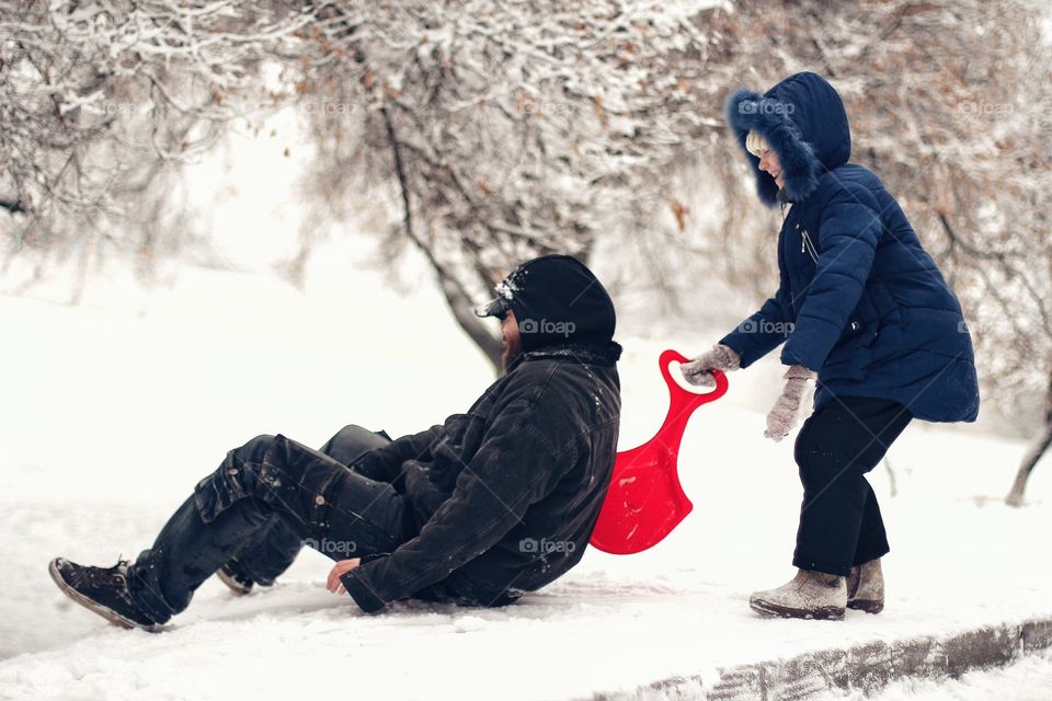 Daughter pushes dad to ride a snow slide