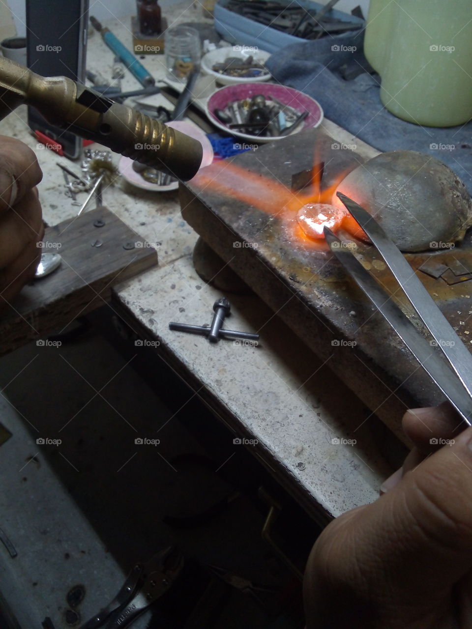 metal plata siendo calentado con soplete al rojo vivo en un taller de joyería para la elaboración de piezas o joyas.